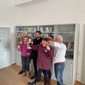 Auf dem Bild sind Mitglieder der Jostiband und der Leiter des Lern- und Gedenkorts Schloss Hartheim bei der Übergabe des Buches zu sehen.